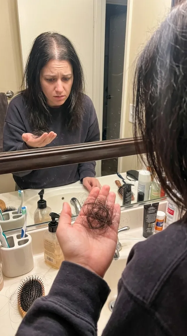 A phone-shot style ad: a woman at a bathroom mirror looking at hair in her hand